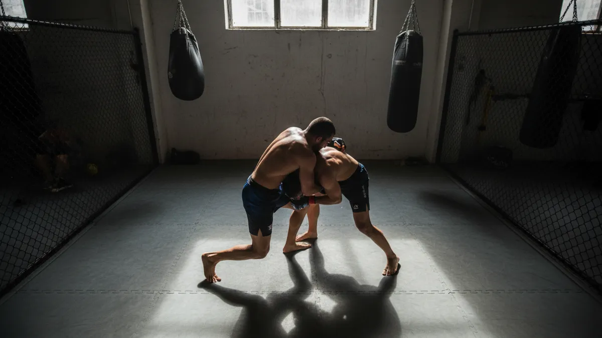 Dos luchadores de UFC forcejean en el suelo, vistos desde arriba.